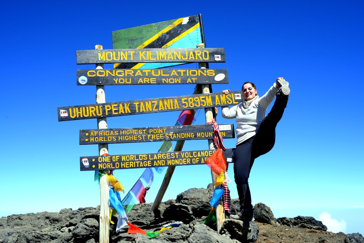 A climber holding a yoga pose at the Uhuru Peak summit sign